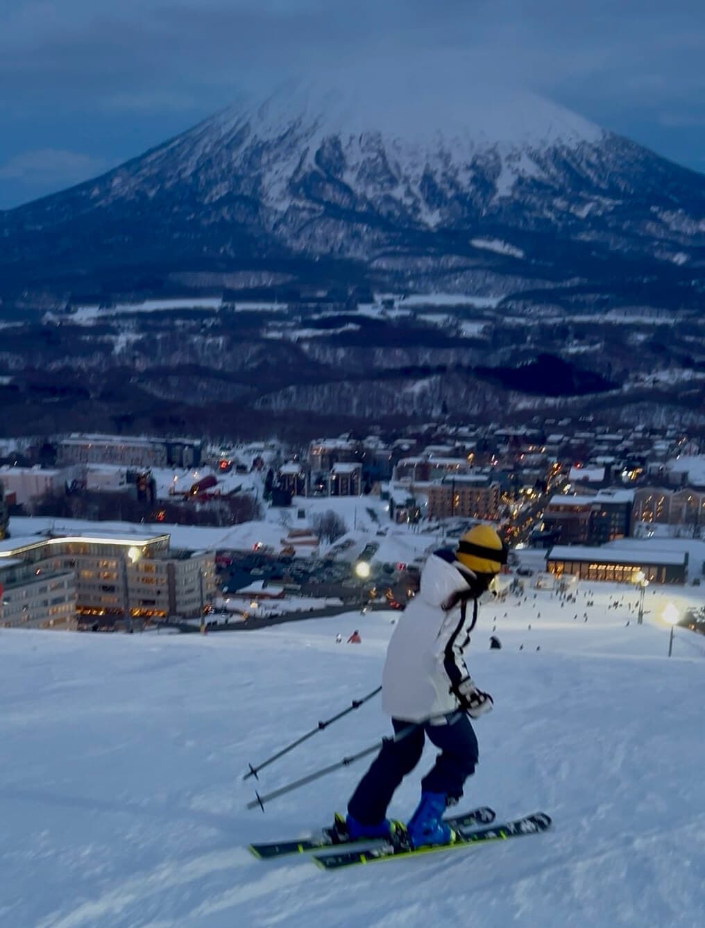 Skier descending toward village lights at dusk